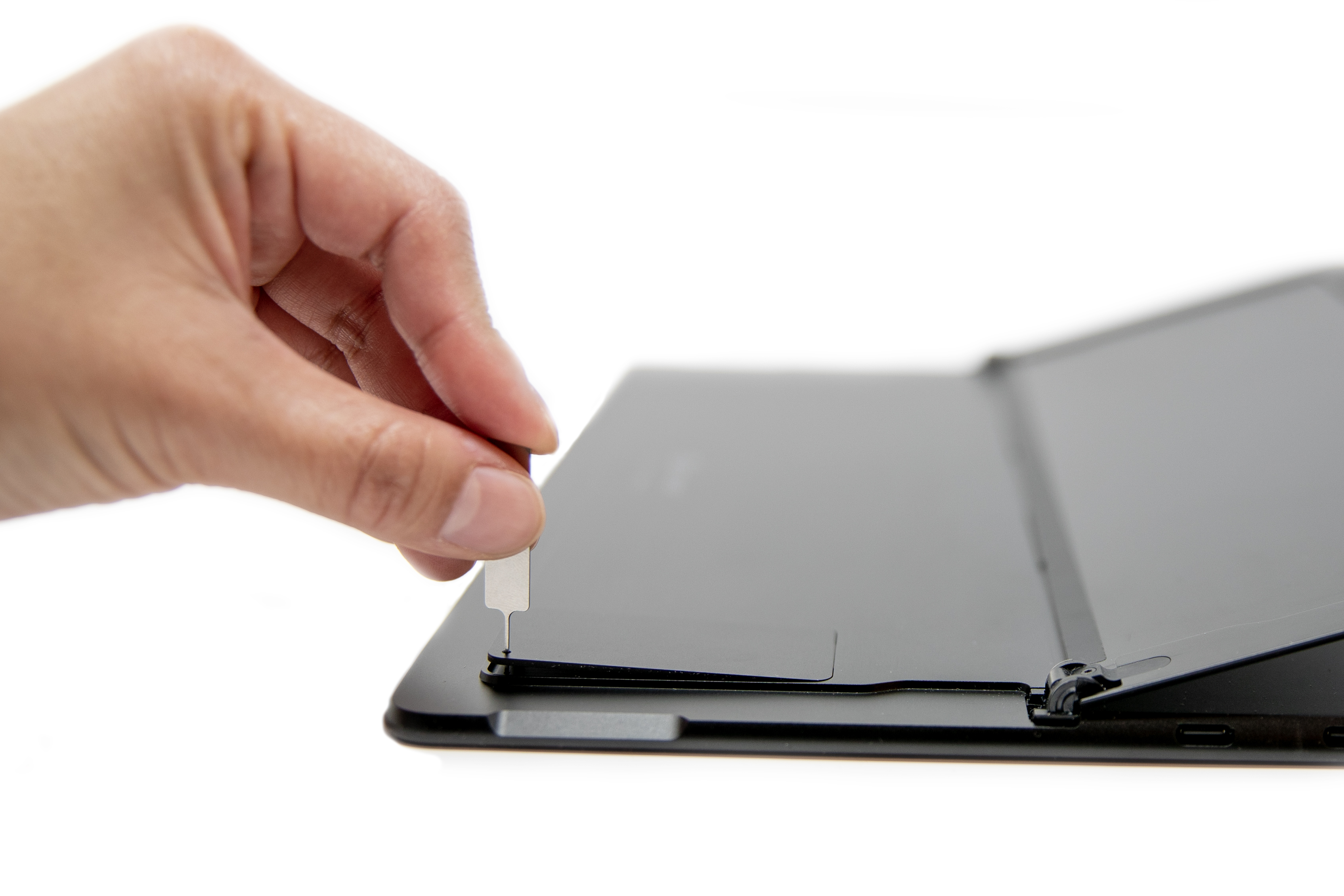 A persons hand inserted a SIM ejector into a Surface Pro X.