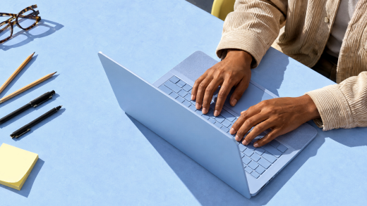 Screenshot that shows a person typing on a laptop at a blue desk.