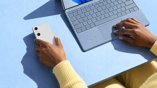 Screenshot shows a person holding a phone next to a laptop.